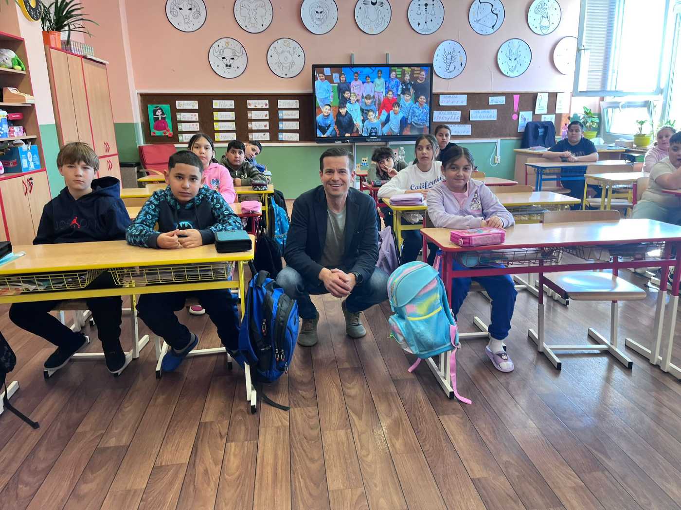 Na snímku jsou žáci základní školy v lavicích. Mezi nimi sedí dětský ombudsman.