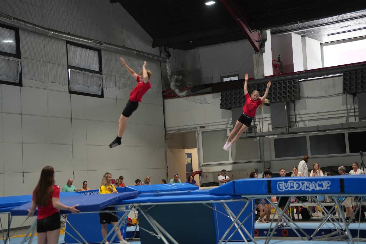Dva sportovci skáčou do výšky na trampolínách.