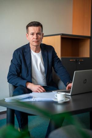 Dětský ombudsman Martin Beneš sedí za stolem. Před sebou má spis a notebook.